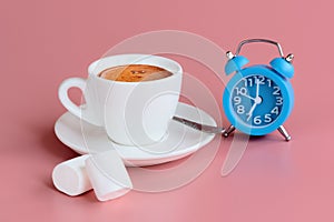 Morning cup of coffee, two marshmallows and blue alarm clock on pink background. Start of the day concept. Copy space