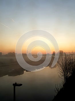 Morning dawns misty with cloudless sky above North London canal and moored boats