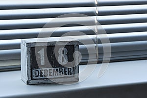 Morning December 18 on wooden calendar standing on window with blinds.