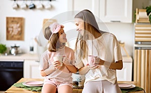 Morning with family. Happy cute little girl with young lovely mom drinking tea in the modern kitchen at home