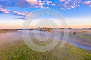 Morning fog in the meadows and at the mouth of the river during sunrise in the countryside, view from the height of the landscape