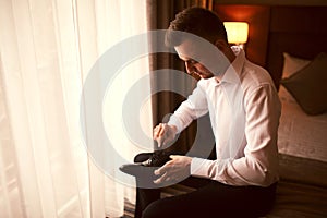 Morning of the groom before the wedding. Groom morning preparation. Young and handsome groom getting dressed in a wedding shoes