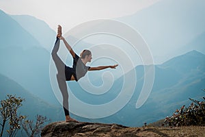 Young woman practices yoga on mountain cliff at sunrise. Mountanious landscape