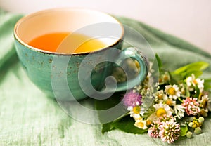 Morning herbal tea cup and summer flowers near window view on blue green cotton napkin background