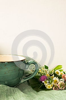 Morning herbal tea cup and summer flowers near window view on blue green cotton napkin background