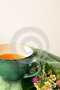 Morning herbal tea cup and summer flowers near window view on blue green cotton napkin background