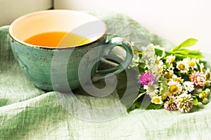 Morning herbal tea cup and summer flowers near window view on blue green cotton napkin background