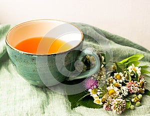 Morning herbal tea cup and summer flowers near window view on blue green cotton napkin background