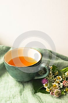 Morning herbal tea cup and summer flowers near window view on blue green cotton napkin background