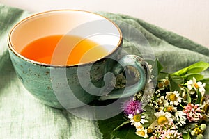 Morning herbal tea cup and summer flowers near window view on blue green cotton napkin background