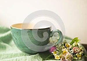 Morning herbal tea cup and summer flowers near window view on blue green cotton napkin background