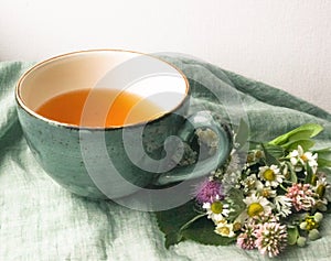 Morning herbal tea cup and summer flowers near window view on blue green cotton napkin background