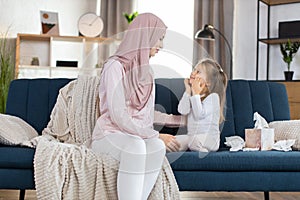 Morning higiene routine at home. Happy Muslim mom in hijab, sits on sofa at cozy room and looks at her cute little photo