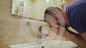 Morning hygiene. Man washes his face with clean water in the bathroom