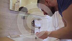 Morning hygiene. Man washes his face with clean water in the bathroom. Slow motion