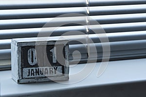 Morning January 01 on wooden calendar standing on window with blinds.