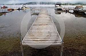 Morning landscape with autumn fog over the lake, a wooden pier and boats on the lake Massavippi, fog and sunlight.