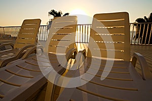 Morning landscape view of empty chaise lounges near swimming pool. Palm trees with blue sea in the background