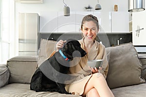 Morning and lifestyle concept. Happy young woman on sofa, sitting with dog, cuddle her puppy and eating cereals, having