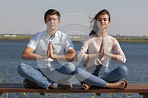 Morning meditation. Beautiful young couple in white clothing meditating outdoors together and keeping eyes closed