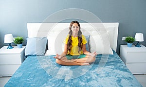 Morning Meditation on bed. Teenager child practicing meditation at bedroom. Relaxed girl on bed in lotus pose and