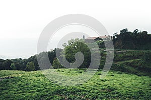 Morning mist in the mountain peaks on natural landscape. Green valley on background foggy dramatic sky, house in horizon