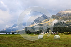 Morning mood at the Sils Lake with rising fog in the mountain, hay bales in the foreground