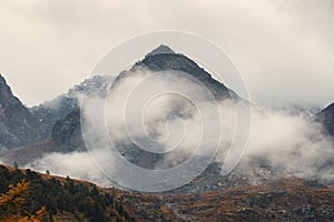 Morning mountain background. Dramatic fog among giant rocky mountains. Ghostly atmospheric view to big cliff. Low clouds and