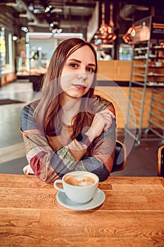 Morning Muse: A Womans Coffee Delight. A woman with long brown hair sits at a cozy coffee shop table, enjoying a cup of