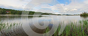 Morning panorama view over lake from fishing place to opposite bank, reflection of sky in the water level.