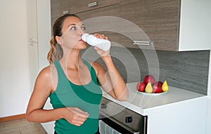 Morning portrait of young woman drinking whey protein beverage. Home fitness girl drinks kefir from bottle photo