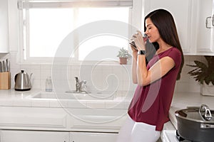 Morning rituals, woman drinking cup of coffee tea in the kitchen next to window with sunlight