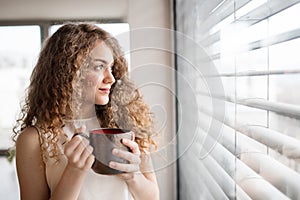 Morning routine for beautiful woman with curly hair drinking cup of coffee.