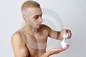 Morning routine. Portrait of handsome young man applying shaving gel, taking care after skin against white studio