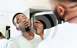 Young black man shaving beard, looking at bathroom mirror