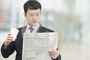 Morning routine of young businessman holding and drinking coffee and reading newspaper