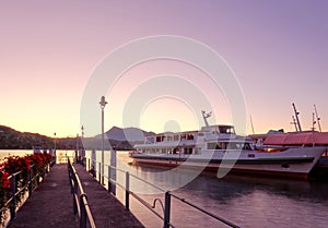 Morning scenery of Lake Lucerne at sunrise with view of a cruise ship parking by a wooden dock