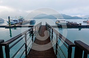 Morning scenery of sightseeing boats moored to the floating docks of a wooden pier & foggy mountains by lakeside