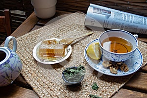 Morning setup on wooden table at balcony, cup of natural tea, teapot, honey, fresh green tea leaves and organic fruits