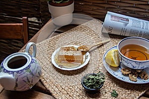 Morning setup on wooden table at balcony, cup of natural tea, teapot, honey, fresh green tea leaves and organic fruits