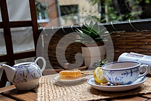 Morning setup on wooden table at balcony, cup of natural tea, teapot, honey, fresh green tea leaves and organic fruits