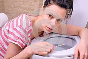 Morning sickness. Young pregnant tired woman is vomiting in toilet at home lookin at camera.