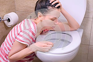 Morning sickness. Young pregnant tired woman is vomiting in toilet sitting on the floor at home.