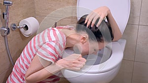 Morning sickness. Young pregnant tired woman is vomiting in toilet sitting on the floor at home.