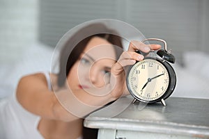 Morning of sleepy young woman turning off alarm clock in bedroom