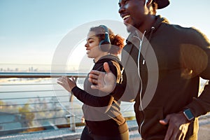 Morning sport. Young smiling african couple in headphones jogging together on the bridge. Happy African man and woman