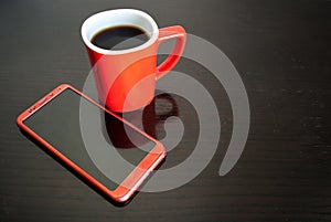 Morning starts from red phone and strong coffee: cup of hot coffee and mobile phone on a dark wooden table