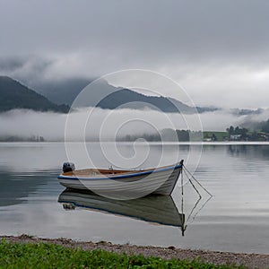 Morning stillness: Fog on the lake, boat, and mountains in the distance.