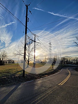 Morning Sun Shine over Field of power lines at the end of a Country road