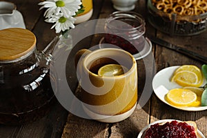 Morning tea party. Mug of tea with lemon, teapot and sweet food on wooden table.